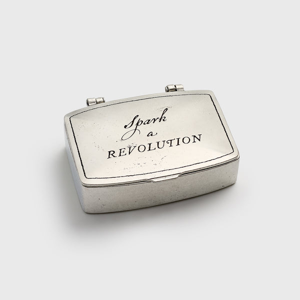 Silver matchbox with 'Spark a Revolution' text on a white background